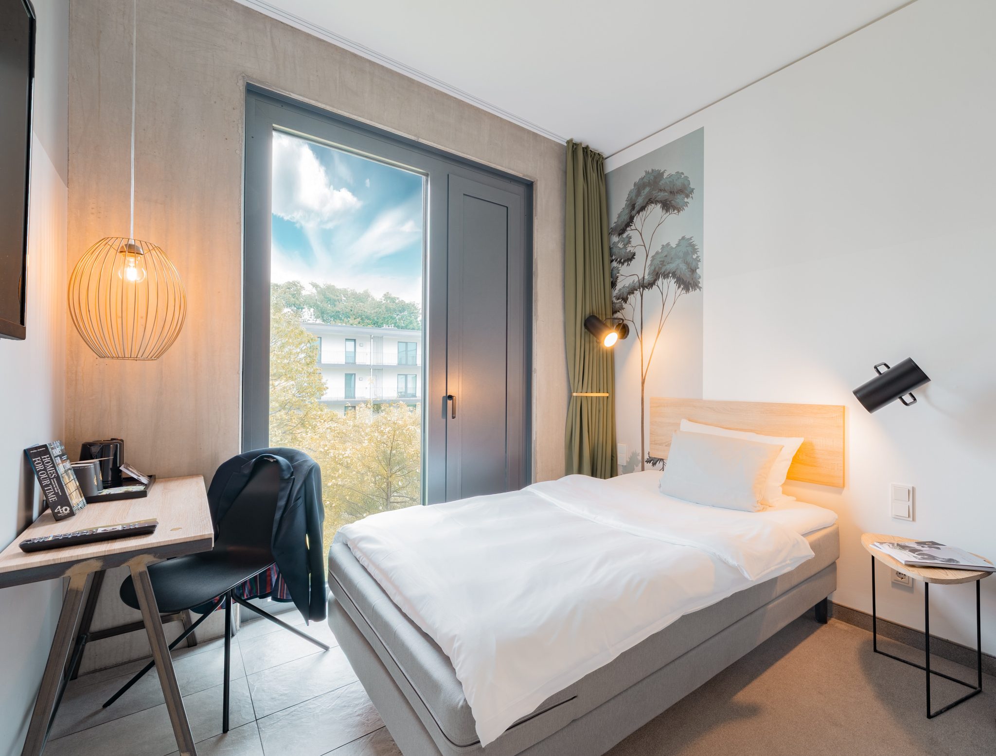 Compact guest room with a bed, desk and full-height window